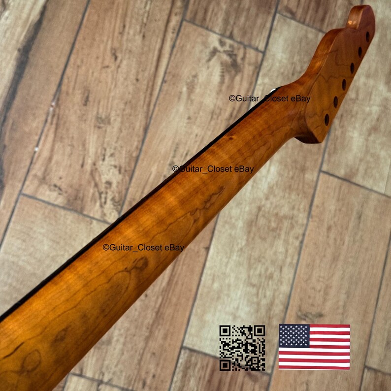 以下が含まれることがあります： 自然な木材仕上げのギターネック。ペグ穴のあるヘッドストックが特徴です。ネックの背面には濃いストライプがあり、明るい茶色です。画像にはQRコードとアメリカ国旗が含まれています。