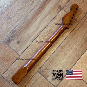 May include: A wooden guitar neck with a natural finish. The neck has a headstock with six tuning peg holes and a smooth, polished surface. The wood grain is visible, and the neck appears to be new. The image includes a QR code and an American flag.