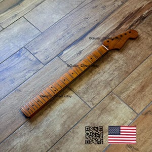 Puede incluir: Un m&aacute;stil de guitarra nuevo, sin terminar, hecho de madera marr&oacute;n claro. El m&aacute;stil tiene un clavijero con agujeros para las clavijas y un diapas&oacute;n con trastes met&aacute;licos. La veta de la madera es visible. La imagen incluye un c&oacute;digo QR y una bandera americana.