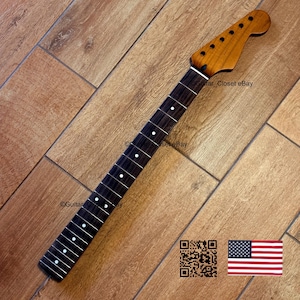 May include: A guitar neck with a dark fretboard and a light brown headstock. The fretboard has white dot inlays. The headstock has tuning peg holes. The image includes a QR code and an American flag.