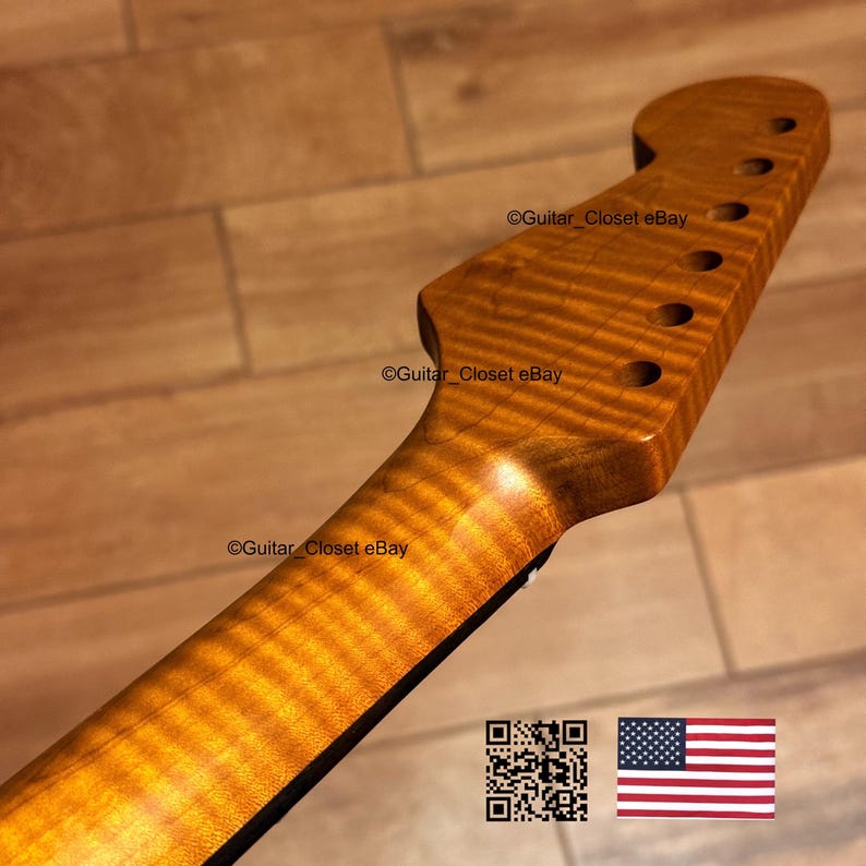 May include: A close-up of a guitar neck with a flamed maple finish. The wood grain has a wavy pattern with a golden-brown color. The headstock has six tuning peg holes. The text "Guitar Closet eBay" is visible.