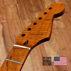 May include: A close-up of a guitar neck with a natural wood finish. The headstock has six tuning peg holes and a curved shape. The neck has a white fretboard and a silver string. The text "Guitar_Closet eBay" is visible.