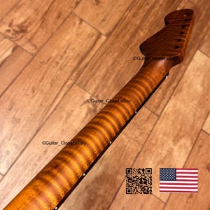 May include: A guitar neck crafted from brown flamed maple wood featuring a distinct tiger-stripe grain pattern. The headstock is angled with six tuner holes, and the side of the fretboard displays small white position markers along the edge.