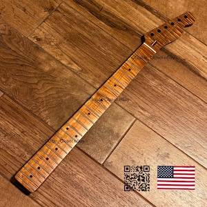 Pu&ograve; includere: Un manico per chitarra caratterizzato da una venatura del legno di acero fiammato marrone chiaro con finitura naturale. Il manico include una tastiera con segnatasti circolari scuri, tasti in metallo e una paletta con fori.