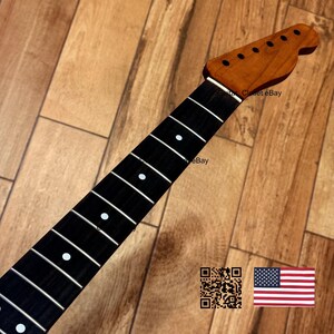 May include: A guitar neck with a dark fretboard and white dot inlays. The headstock is a lighter wood color with tuning peg holes. The neck is set against a wooden background. The image includes a QR code and a US flag.