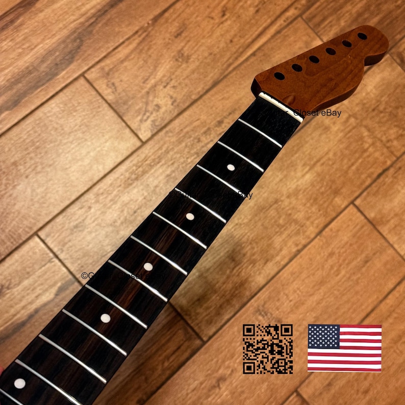 May include: A guitar neck featuring a dark brown wooden headstock with six tuning peg holes and a dark, grained fretboard. The fretboard includes silver metal frets and white circular position markers. The neck is shown at an angle.
