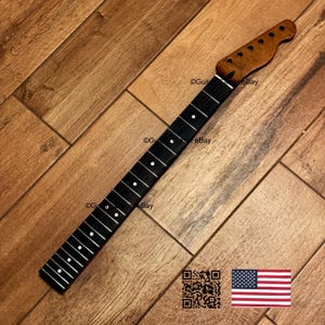 May include: A guitar neck with a dark fretboard and a light-colored headstock. The fretboard has white dot inlays. The headstock is a lighter brown color. The neck is set against a wooden background. The image includes a QR code and an American flag.