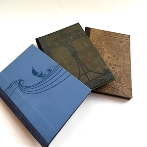 May include: Three vintage hardcover books with different designs. The book on the left has a blue cover with a wave and a sailboat design. The book in the middle has a green cover with the text "The Beacon Fifth Reader". The book on the right has a brown cover with the text "Alta Edition".