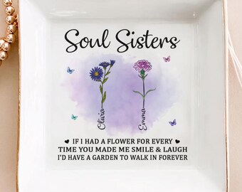 May include: A square, white ceramic trinket dish with gold trim. The dish features the text "Soul Sisters" above two floral illustrations and the names "Olivia" and "Emma". The text below reads: "IF I HAD A FLOWER FOR EVERY TIME YOU MADE ME SMILE & LAUGH I'D HAVE A GARDEN TO WALK IN FOREVER."