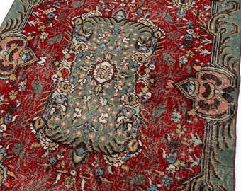 May include: A rectangular area rug featuring a deep red background with a central sage green medallion. The rug is decorated with intricate floral and vine patterns in shades of cream, light blue, and dark brown, framed by a wide sage green border.