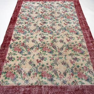 May include: Rectangular floral rug with a cream-colored background and a burgundy border. The rug features a pattern of pink, blue, and purple flowers and green leaves. The rug is a large size.