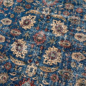 May include: A rectangular area rug featuring a deep blue background with an intricate pattern of floral motifs, paisley shapes, and scrolling vines in shades of cream, muted red, and dark brown, with a distressed, weathered texture throughout.