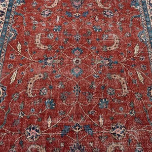 May include: A distressed, rectangular rug with a rich red background and intricate floral patterns in blue, beige, and cream. The rug features a detailed border with similar floral motifs, creating a classic, vintage aesthetic.