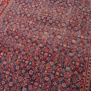 May include: A rectangular area rug featuring a dense, intricate pattern of floral and geometric motifs in shades of deep navy blue, crimson red, and muted beige. The design includes a wide, ornate border with repeating floral elements.