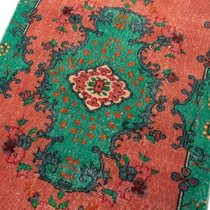 May include: A rectangular runner rug featuring a vibrant coral-orange central field and a bright green border. The design includes a dark charcoal floral vine pattern, a central geometric medallion, and small clusters of pink and orange flowers.
