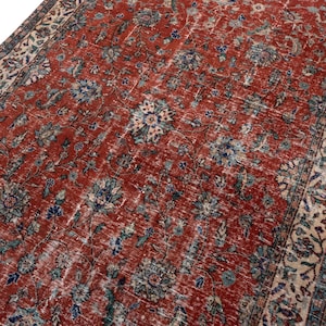 May include: A rectangular area rug featuring a deep red field covered in an intricate floral pattern with blue, cream, and dark green accents. The rug is framed by a wide, ornate border containing repeating botanical motifs in matching colors.