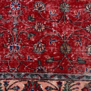 K&ouml;nnte beinhalten: Nahaufnahme eines roten, abgenutzten Teppichs mit floralen Mustern. Der Teppich hat ein rotes Mittelfeld mit verblassten Blumenmotiven in Beige, Blau und Gr&uuml;n. Ein Rand in einem helleren Beigeton umrahmt den Teppich.