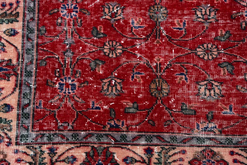 K&ouml;nnte beinhalten: Nahaufnahme eines roten, abgenutzten Teppichs mit floralen Mustern. Der Teppich hat ein rotes Mittelfeld mit verblassten Blumenmotiven in Beige, Blau und Gr&uuml;n. Ein Rand in einem helleren Beigeton umrahmt den Teppich.