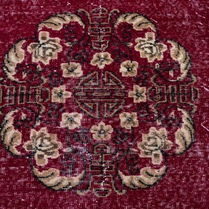 May include: A close-up of a red rug with an ornate floral design. The central motif features a symmetrical arrangement of flowers and geometric shapes in beige and dark brown. The rug has a distressed, vintage appearance.