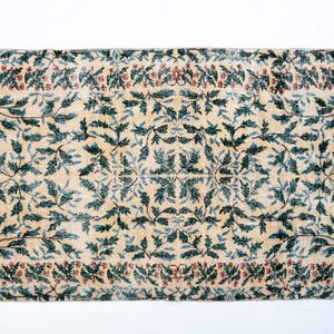 May include: Rectangular rug with a cream-colored background and a repeating pattern of teal-colored leaves and red berries. The border features a similar design, creating a cohesive look. The rug's design is symmetrical.
