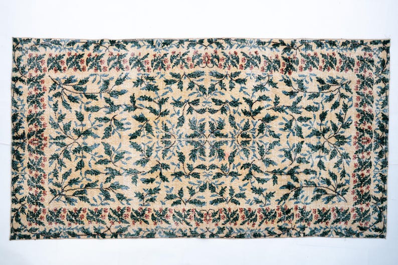 May include: Rectangular rug with a cream-colored background and a repeating pattern of teal-colored leaves and red berries. The border features a similar design, creating a cohesive look. The rug's design is symmetrical.