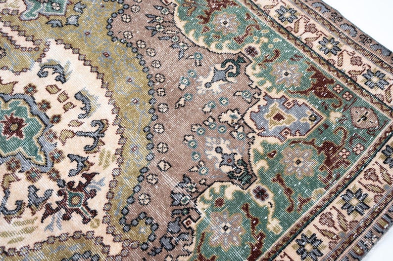 May include: A woven area rug featuring a complex pattern of floral and geometric motifs in shades of sage green, dusty rose, cream, and slate blue. The design includes a central field with intricate borders and a distressed, weathered texture.