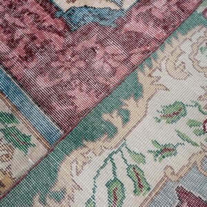 May include: Close-up of a section of a vintage rug with a patchwork design. The rug features floral and geometric patterns in shades of burgundy, teal, green, and cream. The texture appears soft and worn, suggesting age and use.