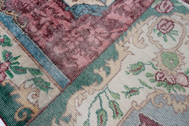 May include: Close-up of a section of a vintage rug with a patchwork design. The rug features floral and geometric patterns in shades of burgundy, teal, green, and cream. The texture appears soft and worn, suggesting age and use.