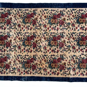 May include: Rectangular rug with a cream-colored field featuring a floral pattern in burgundy, teal, and gold. The rug has a dark blue border. The floral design includes roses and other flowers.
