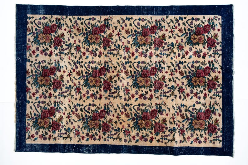 May include: Rectangular rug with a cream-colored field featuring a floral pattern in burgundy, teal, and gold. The rug has a dark blue border. The floral design includes roses and other flowers.