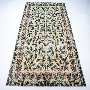 May include: Rectangular rug with a cream-colored background and a repeating pattern of green leaves and red flowers. The rug has a border of red flowers and green leaves.