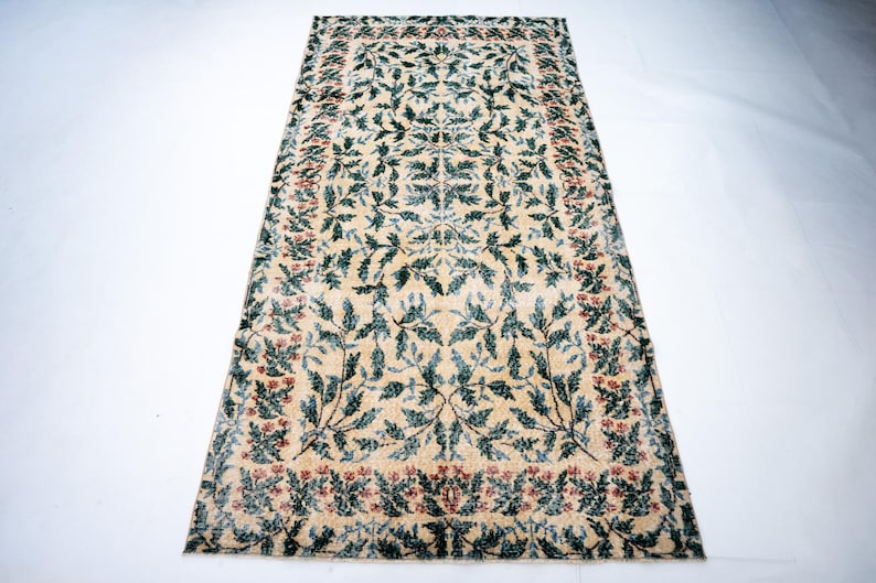 May include: Rectangular rug with a cream-colored background and a repeating pattern of green leaves and red flowers. The rug has a border of red flowers and green leaves.