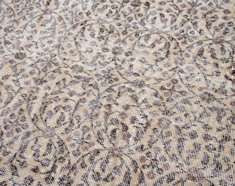 May include: Close-up of a beige and brown patterned rug. The rug features a detailed floral design with a distressed, vintage appearance. The color palette includes beige, brown, and hints of purple.