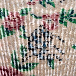 Pode incluir: Close-up de um tapete bege com um padr&atilde;o floral. O tapete apresenta desenhos repetidos de flores cor-de-rosa com folhas e caules verdes. Um elemento de design central tem detalhes em azul e preto.