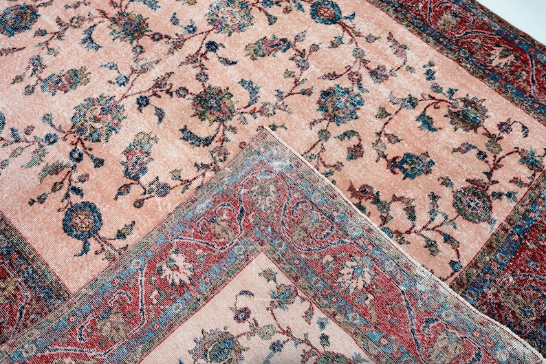 Pu&ograve; includere: Due tappeti antichi con motivi floreali. I tappeti hanno uno sfondo color pesca con disegni floreali blu e verdi. I bordi sono rossi e blu con motivi intricati. I tappeti sono piegati l'uno sull'altro.