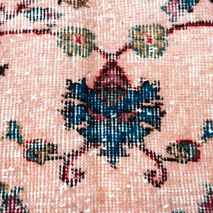Pu&ograve; includere: Primo piano di un tappeto vintage con un motivo floreale dettagliato. Il tappeto presenta uno sfondo color pesca chiaro con disegni intricati in verde acqua, bordeaux e verde oliva. Il motivo centrale &egrave; una composizione floreale stilizzata.