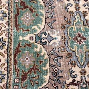 May include: A woven rug featuring a complex pattern with a cream-colored background, sage green floral medallions, and deep maroon accents. The border displays a repeating geometric motif in blue, brown, and cream, creating a dense, textured surface.