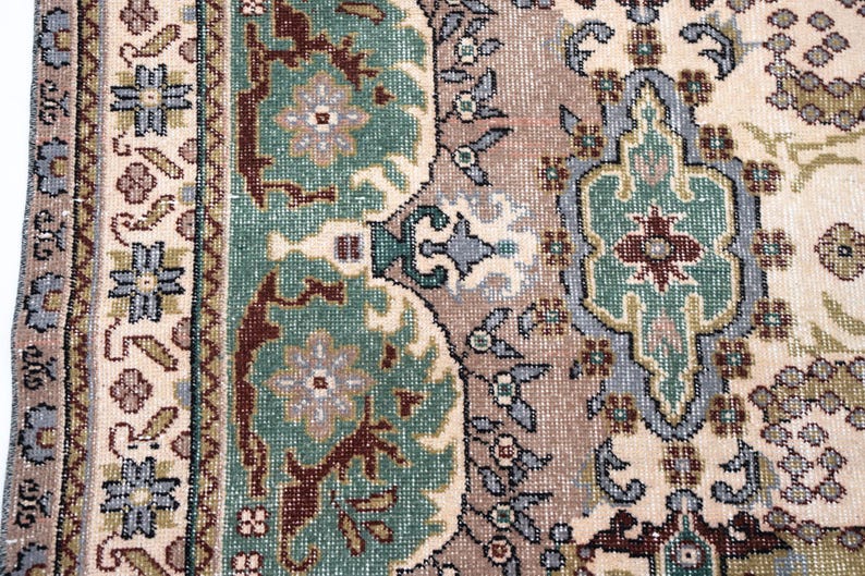 May include: A woven rug featuring a complex pattern with a cream-colored background, sage green floral medallions, and deep maroon accents. The border displays a repeating geometric motif in blue, brown, and cream, creating a dense, textured surface.