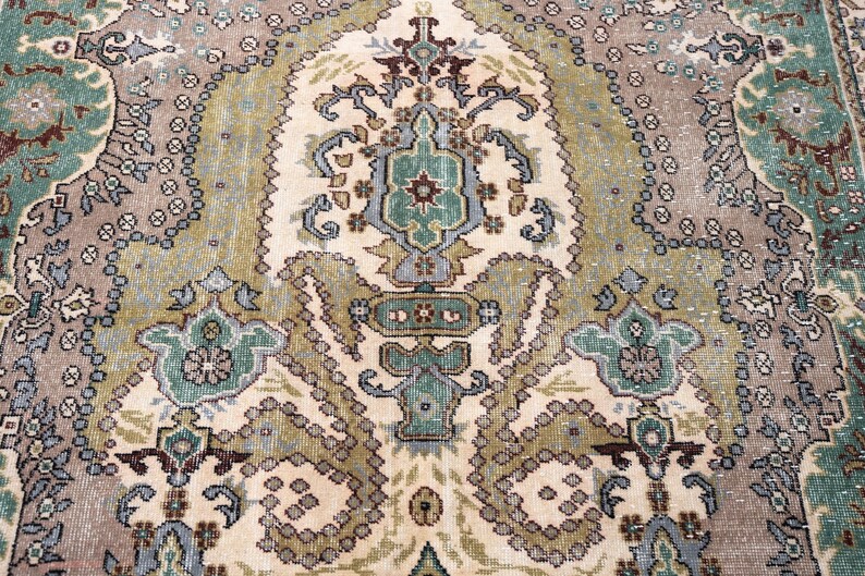 May include: A woven area rug featuring a central medallion and intricate floral motifs in shades of sage green, dusty rose, cream, and slate blue. The design includes symmetrical patterns with detailed borders and a weathered, textured appearance.