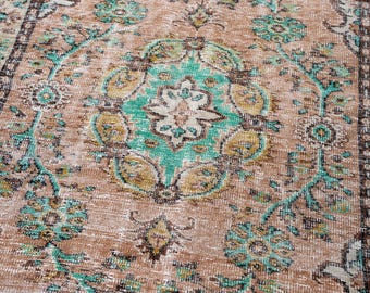 May include: A distressed, vintage-style rug with a central medallion design. The rug features a warm, earthy color palette with shades of brown, beige, and accents of teal and gold. Floral and geometric patterns create an antique aesthetic.