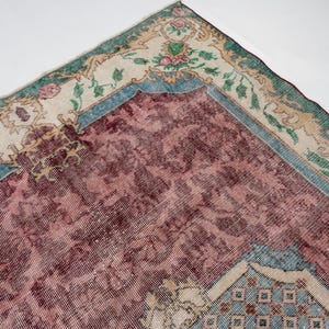 May include: An antique rug with a distressed, vintage appearance. The rug features a central field of deep burgundy, framed by a border of cream, teal, and green. Floral and geometric patterns adorn the rug's surface, creating a classic, timeless aesthetic.