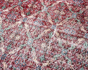 May include: Close-up of a distressed, vintage rug with a detailed floral pattern. The rug features a rich red background with accents of blue, green, and cream. The design is intricate and appears worn, giving it a classic, antique look.