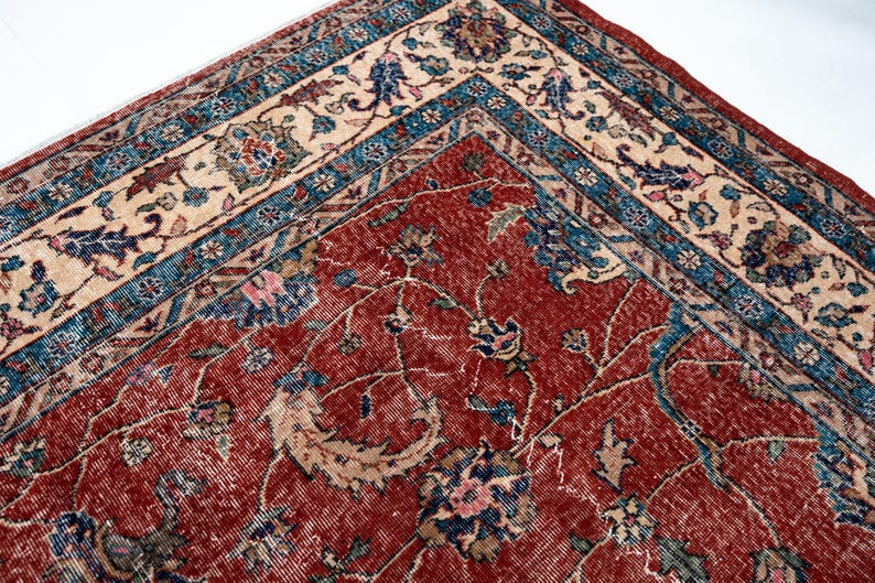 May include: Close-up of a section of a vintage rug with a detailed floral pattern. The rug features a deep red central field with intricate designs in blue, beige, and pink. The border has a contrasting beige and blue pattern.