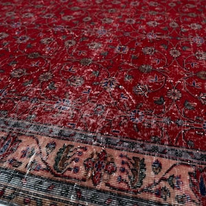 K&ouml;nnte beinhalten: Ein roter, abgenutzter Teppich mit einem komplizierten Blumenmuster. Der Teppich hat einen detaillierten Rand mit floralen und geometrischen Designs in Beige-, Blau- und Gr&uuml;nt&ouml;nen. Die Oberfl&auml;che des Teppichs hat ein abgenutztes, Vintage-Aussehen.