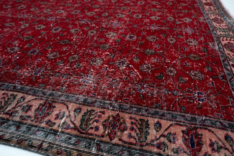 K&ouml;nnte beinhalten: Ein roter, abgenutzter Teppich mit einem komplizierten Blumenmuster. Der Teppich hat einen detaillierten Rand mit floralen und geometrischen Designs in Beige-, Blau- und Gr&uuml;nt&ouml;nen. Die Oberfl&auml;che des Teppichs hat ein abgenutztes, Vintage-Aussehen.