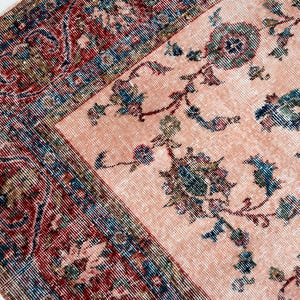 Pu&ograve; includere: Due tappeti antichi con motivi floreali. Un tappeto ha un campo color salmone con accenti floreali blu e verdi. L'altro tappeto ha un bordo rosso, blu e marrone con un design dettagliato. I tappeti sono posizionati ad angolo.