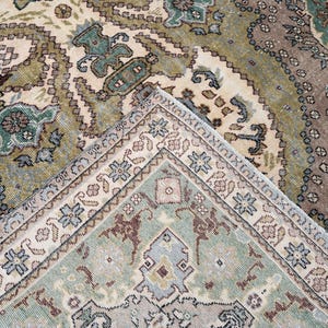 May include: A woven area rug featuring an intricate pattern of floral and geometric motifs in shades of sage green, dusty rose, cream, and slate blue. The design includes a central field with a detailed border, showcasing a dense, symmetrical layout.