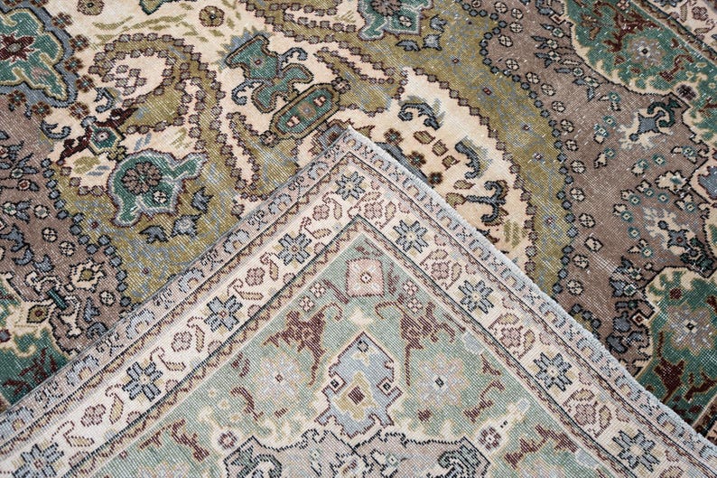 May include: A woven area rug featuring an intricate pattern of floral and geometric motifs in shades of sage green, dusty rose, cream, and slate blue. The design includes a central field with a detailed border, showcasing a dense, symmetrical layout.