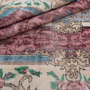 May include: Close-up of a vintage rug with a distressed appearance. The rug features a complex floral pattern in shades of burgundy, teal, cream, and green. The design includes ornate borders and a faded, textured look, suggesting age and use.
