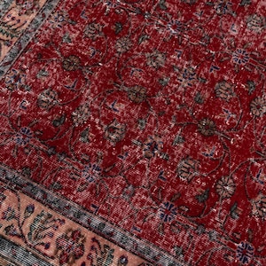 K&ouml;nnte beinhalten: Ausschnitt eines roten, im Used-Look gehaltenen Teppichs mit einem komplizierten Blumenmuster. Der Teppich hat ein verblasstes Aussehen, mit einem Rand, der ein helleres, florales Design aufweist. Die Farbpalette umfasst Rot-, Braun-, Blau- und Beiget&ouml;ne.